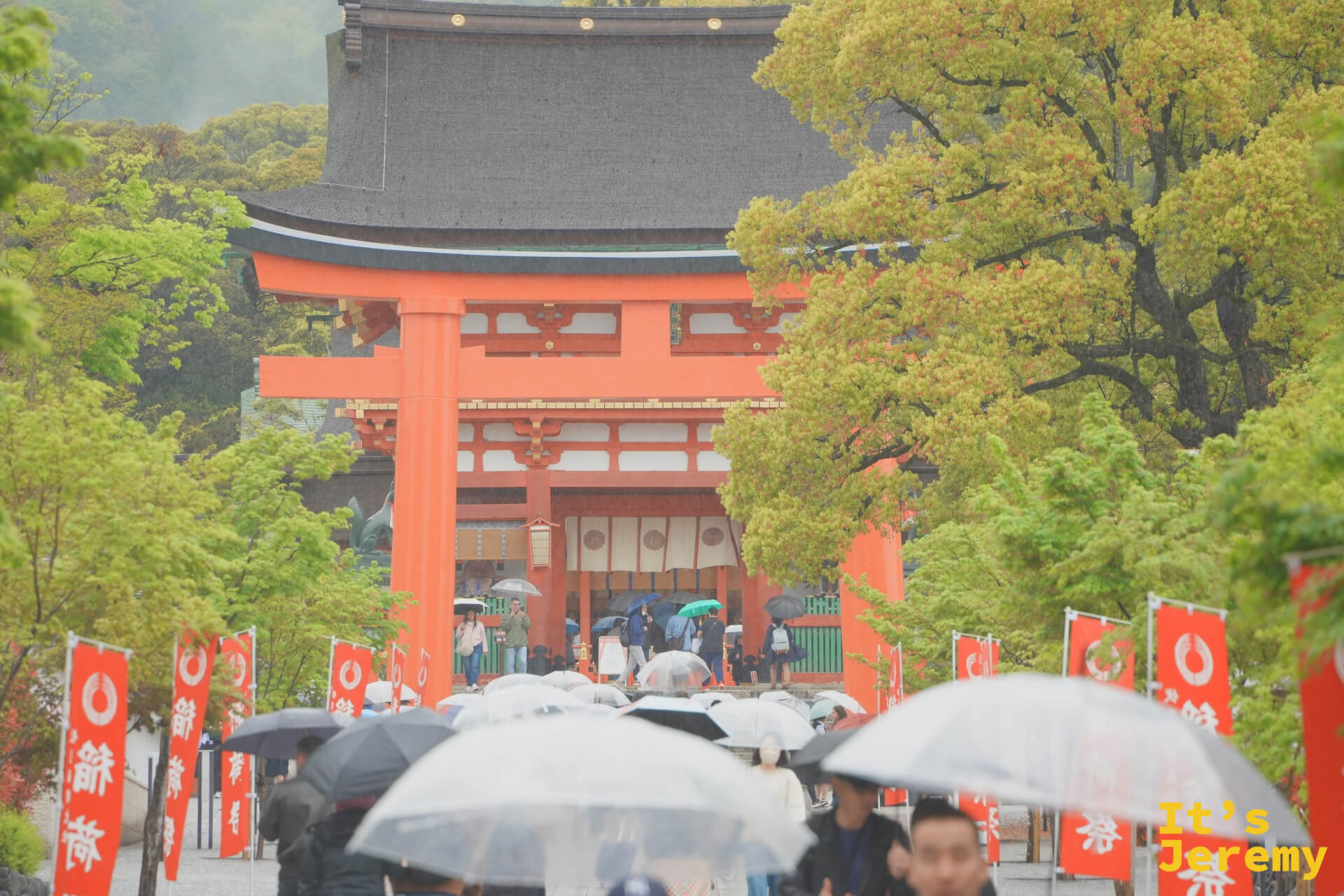 遠景的樓門、鳥居與旗幟，雨中人潮從遠處走來，整個畫面像一張舊明信片