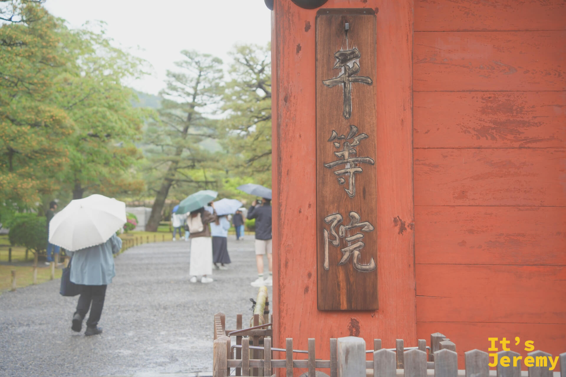平等院入口的朱紅色大門與「平等院」木牌，雨中訪客各撐著傘魚貫而入