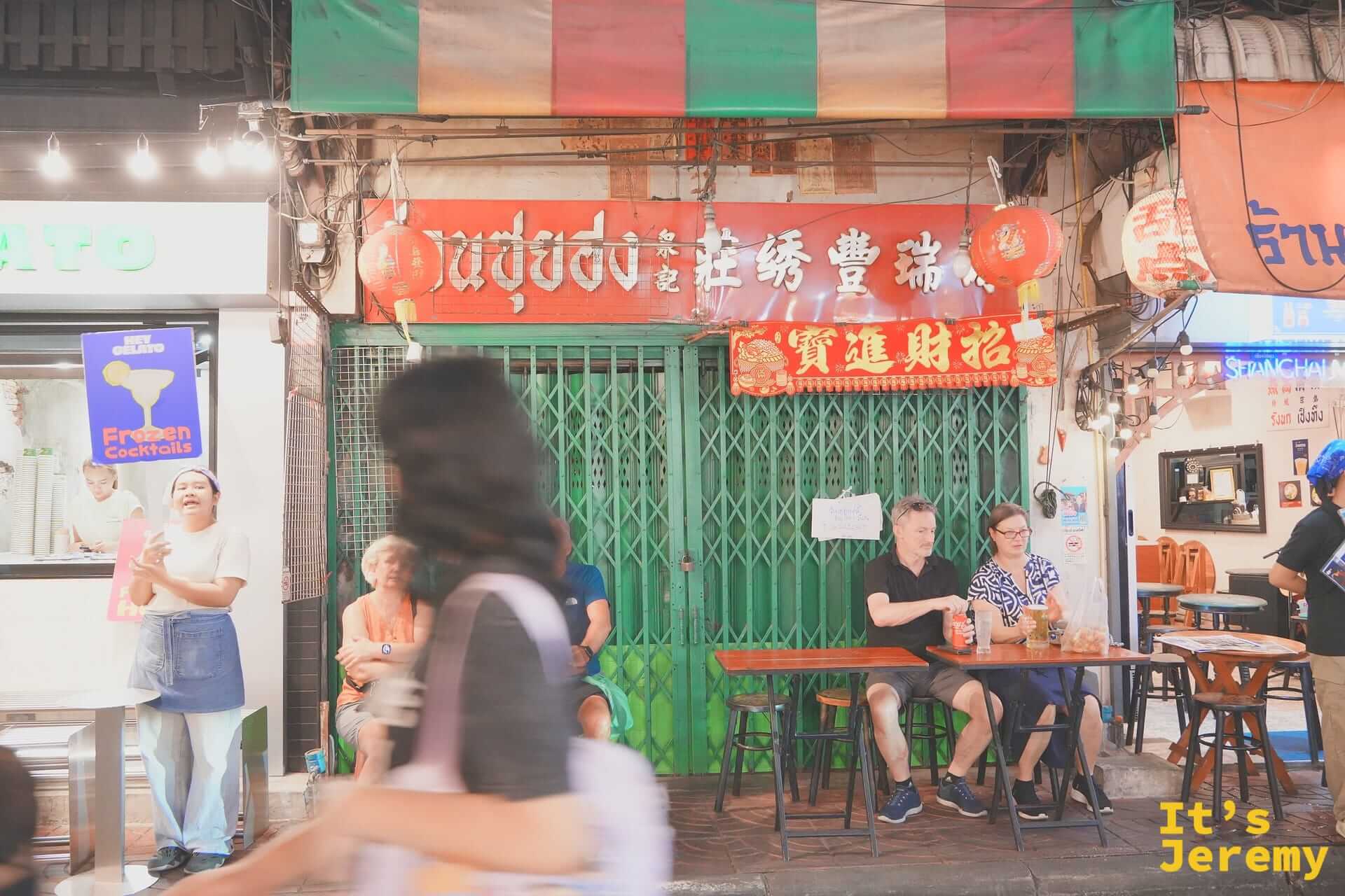 唐人街店家招牌前坐著等餐的外國觀光客
