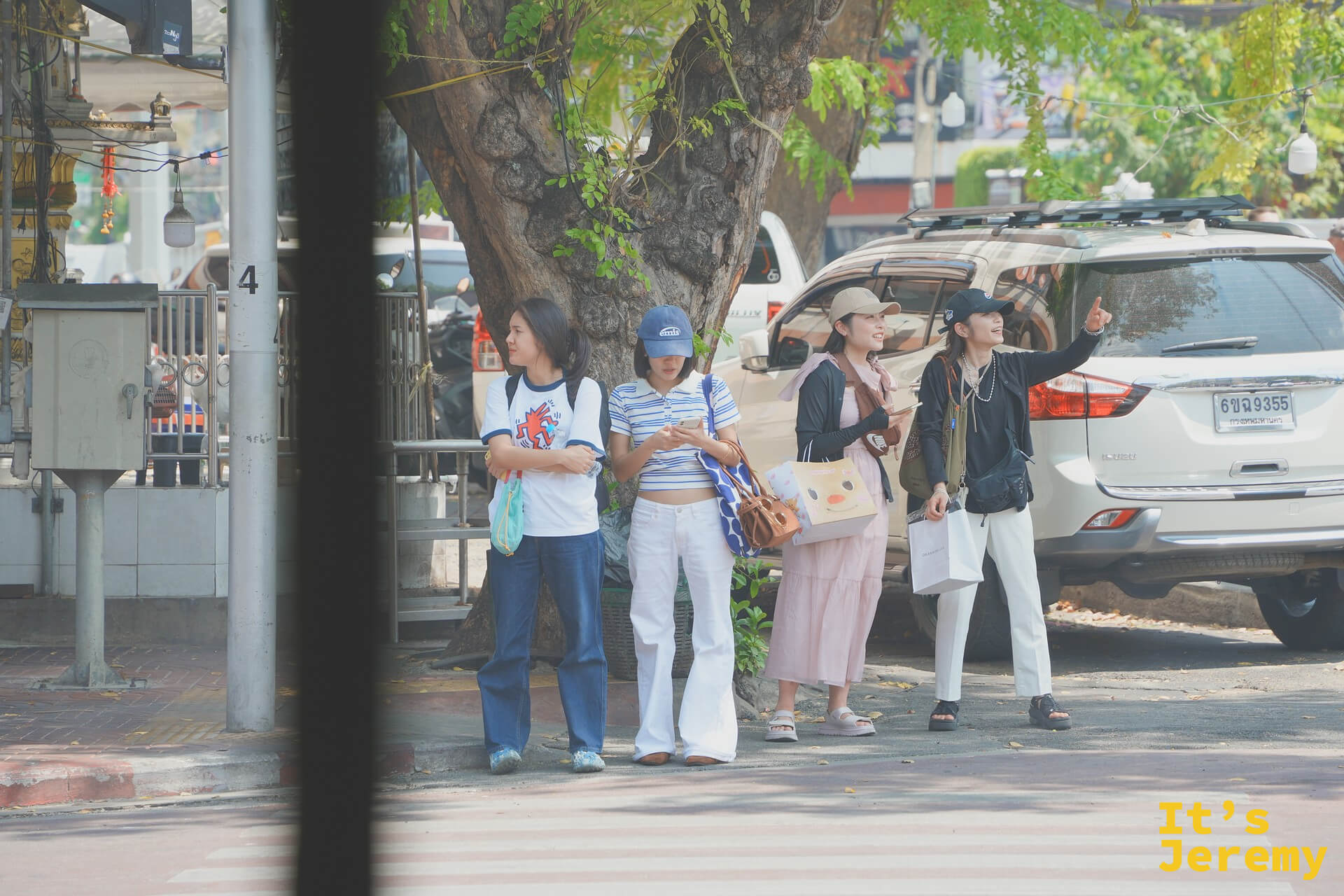 對街四個穿復古丹寧的曼谷女生在樹蔭下伸手攔車，週間下午的老城區一景