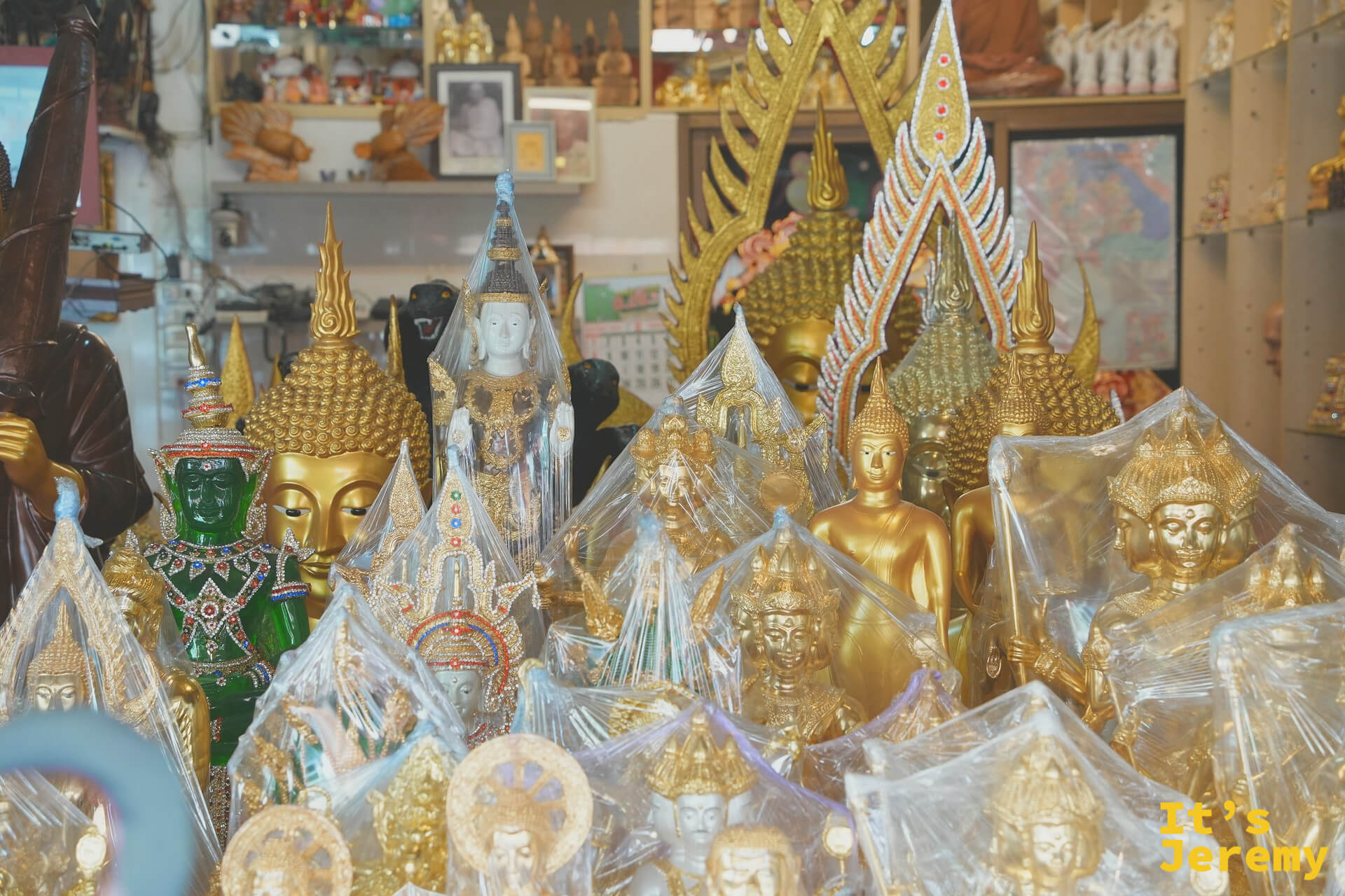 一家佛具店的玻璃窗裡，包好保鮮膜的金佛、綠面神像與佛龕擺得密密麻麻