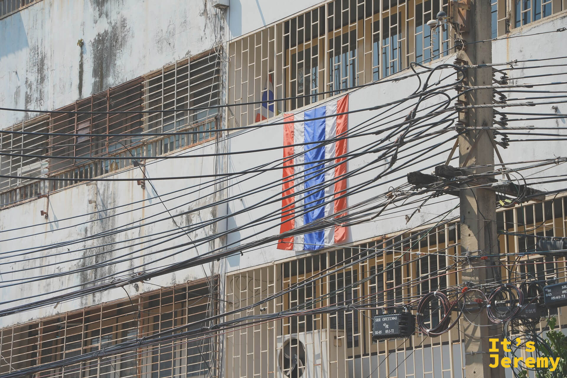 佛具街上的老樓掛著一面褪色泰國國旗，糾結電線一路繞下來