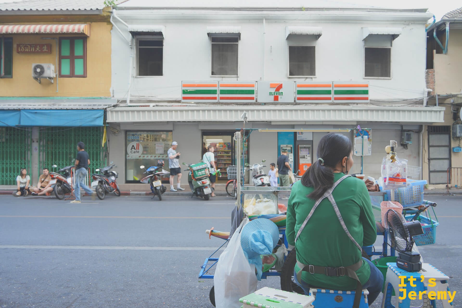 7-Eleven 對街賣涼粉的阿姨推車與背對鏡頭的剪影，便利商店與街邊小販的並存