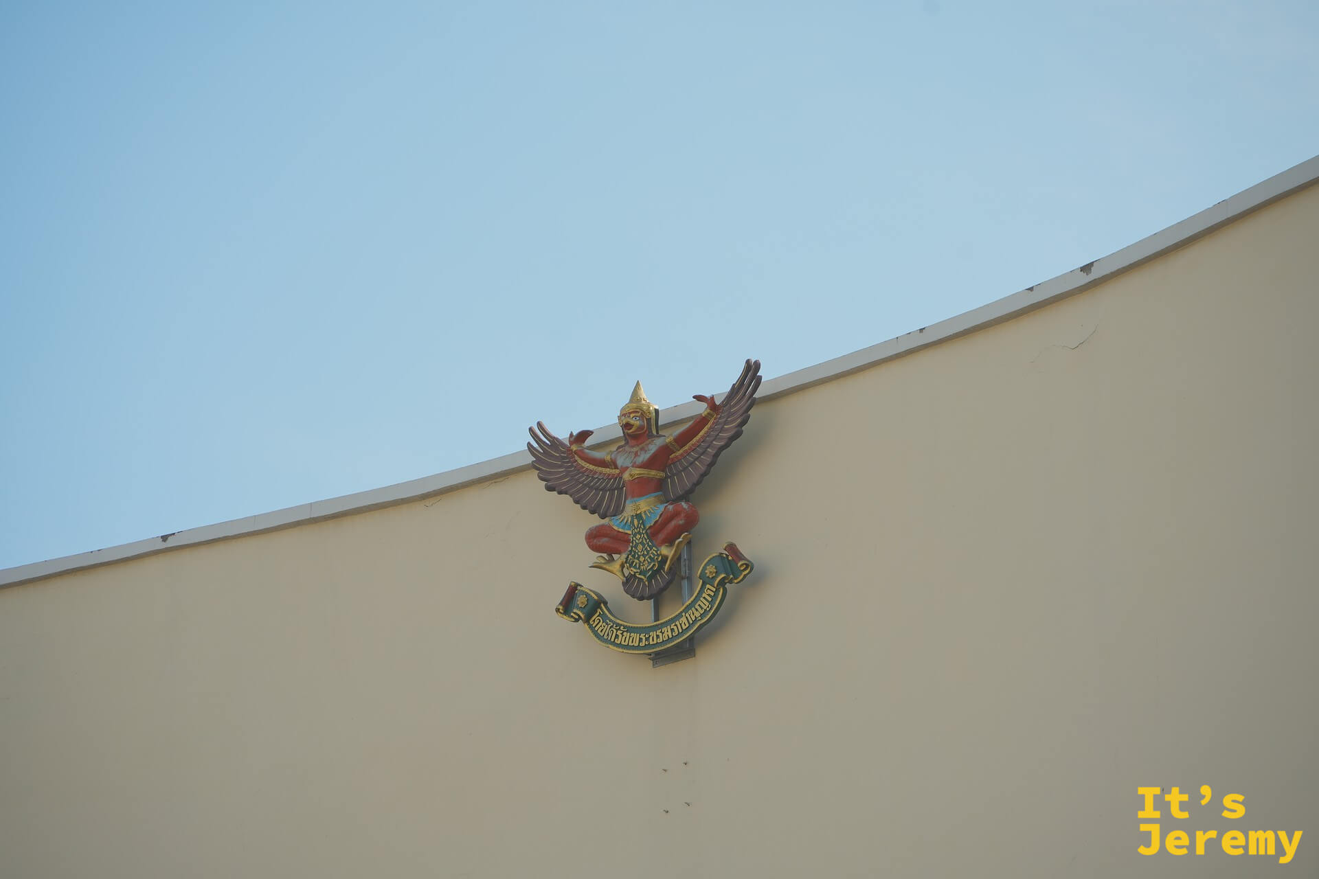 一棟米黃色官方建築外牆掛著的金翅鳥（Garuda）雕飾，這是泰國皇家機構的象徵