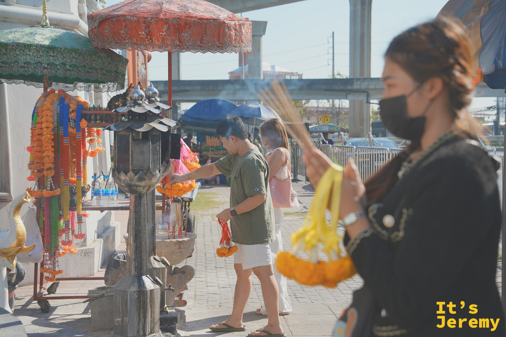 旅客在路邊神龕點線香祈福，背景是 BTS 高架