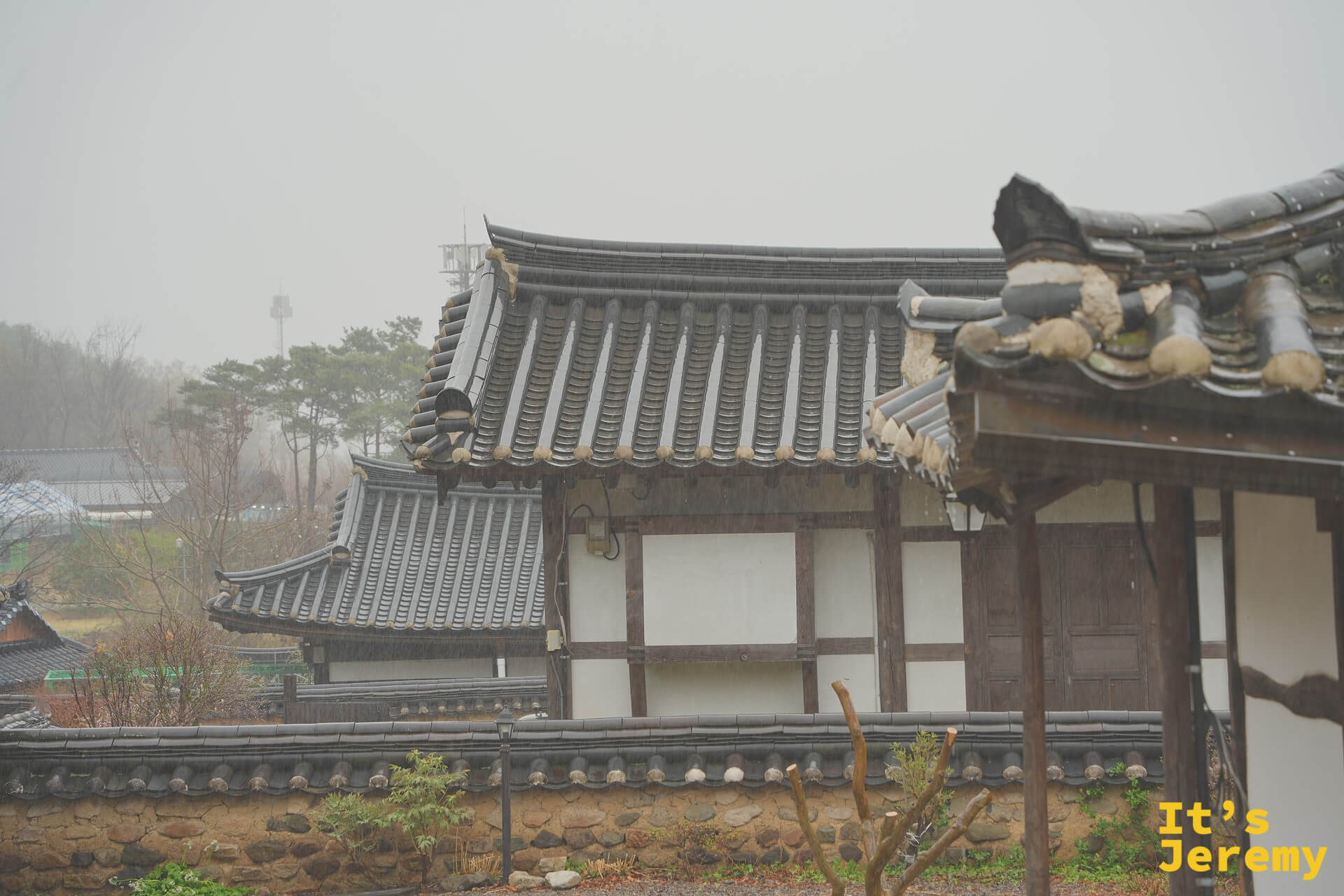雨霧中疊出層次的韓屋屋頂群，遠方山頭隱入低雲，灰白天空讓瓦片顯得格外沉靜