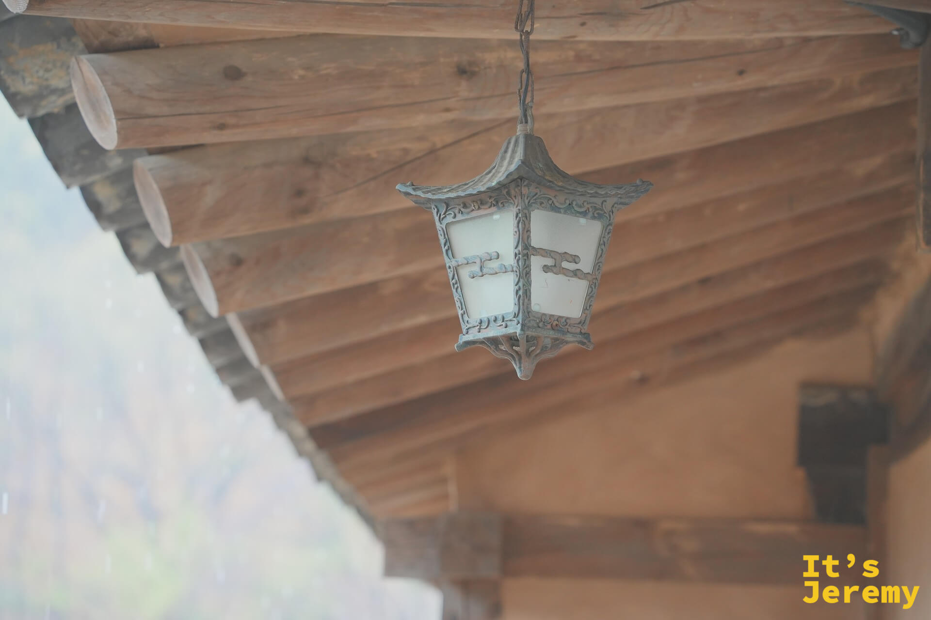 韓屋廊廡下懸掛的傳統宮燈，木紋天花板在雨霧中透著暖意