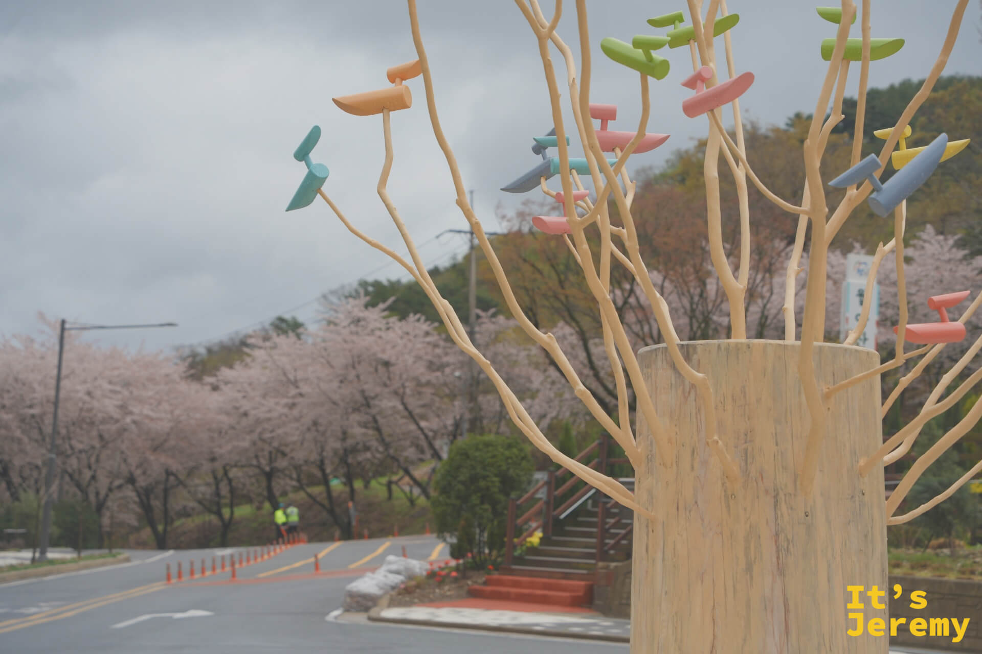 月牙山公園入口旁的彩色枝葉藝術裝置，前景鮮豔，背景是霧中的粉色花道