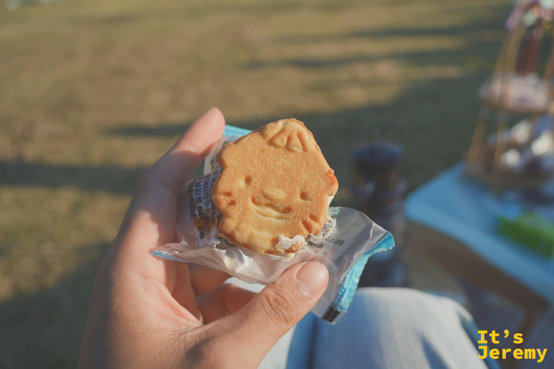 咬開一半的水獺形餅乾,奶油夾心夾在中間,草地與竹籃在遠景帶出野餐的閒適感