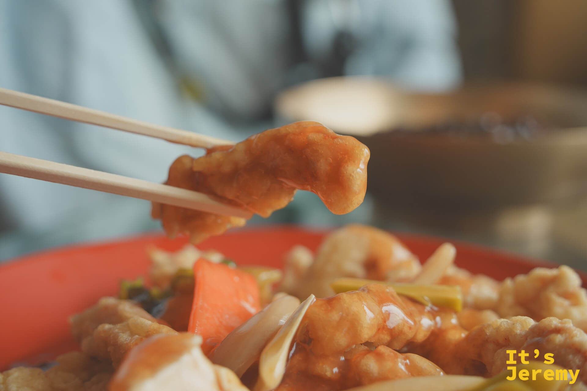 用筷子夾起一塊糖醋肉的特寫，醬汁在燈光下閃閃發亮