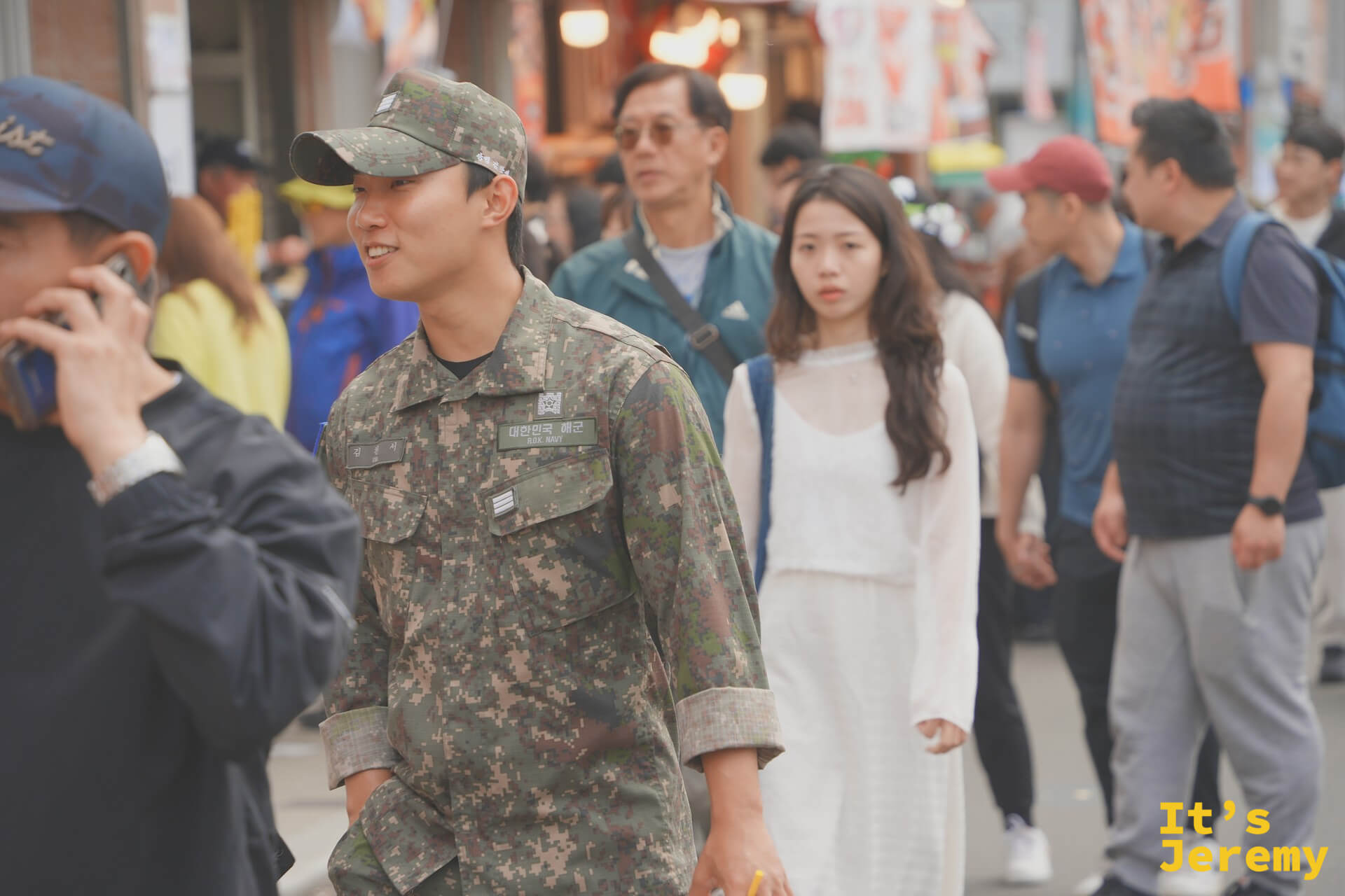 放假的韓國海軍士兵在余佐川花道旁留影，軍服橄欖綠與粉白花廊形成鎮海獨有的組合