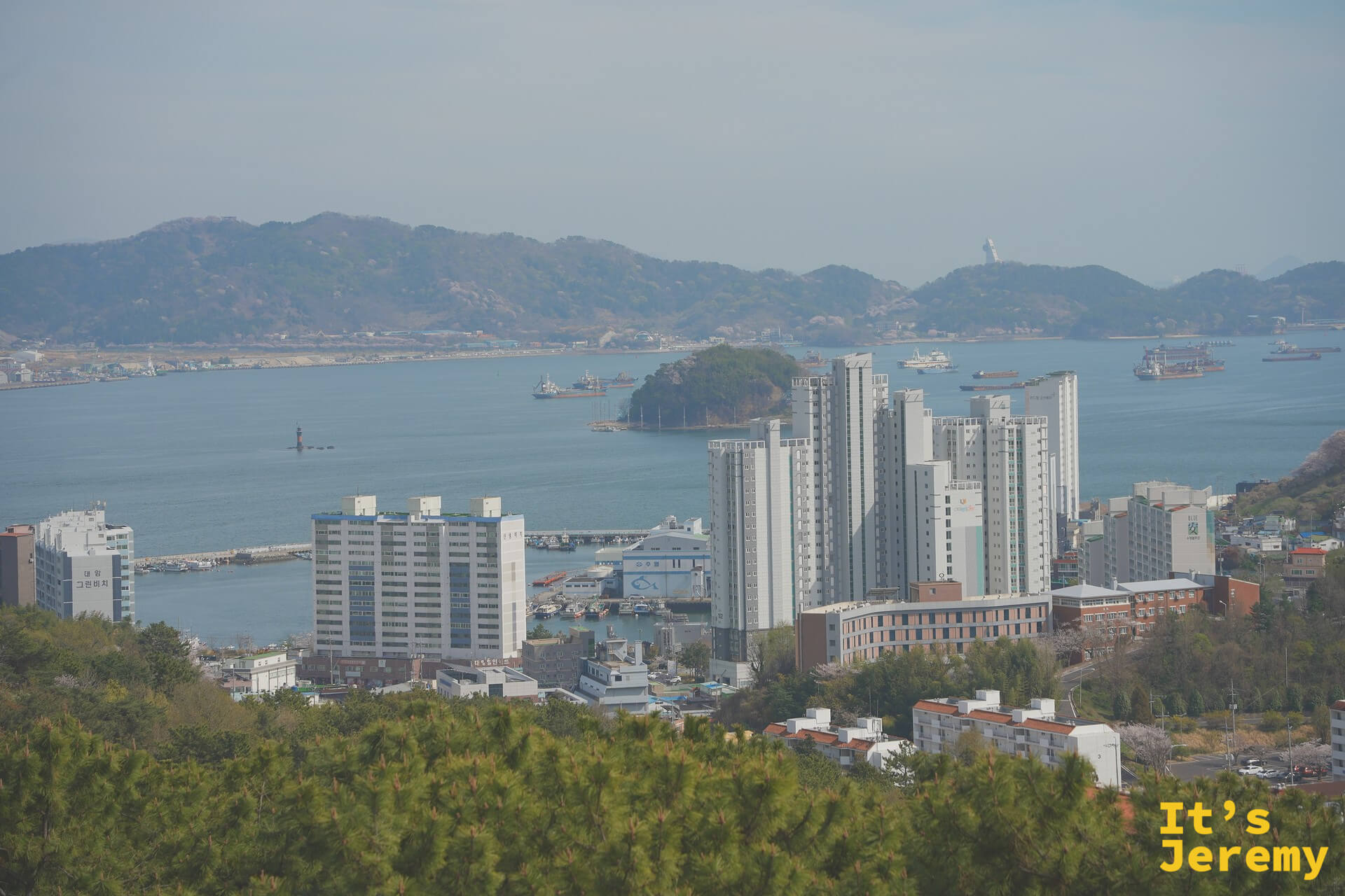 從鎮海塔眺望鎮海港灣,高樓沿海岸林立,遠方群山層疊,海面上可見船隻穿梭出沒