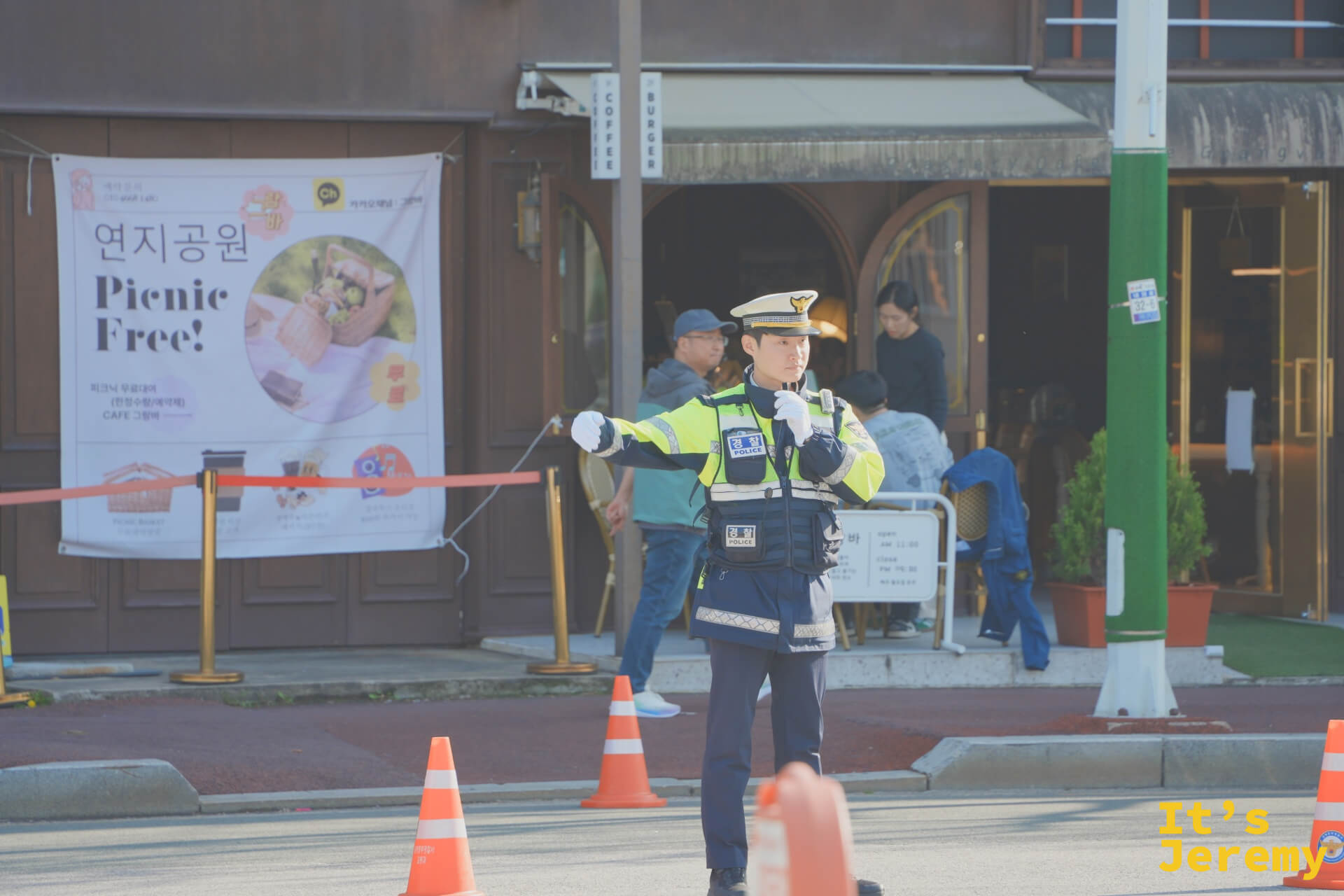 春祭當天公園入口附近，交警指揮交通，後方咖啡館外牆掛著「연지공원 Picnic Free！」活動海報