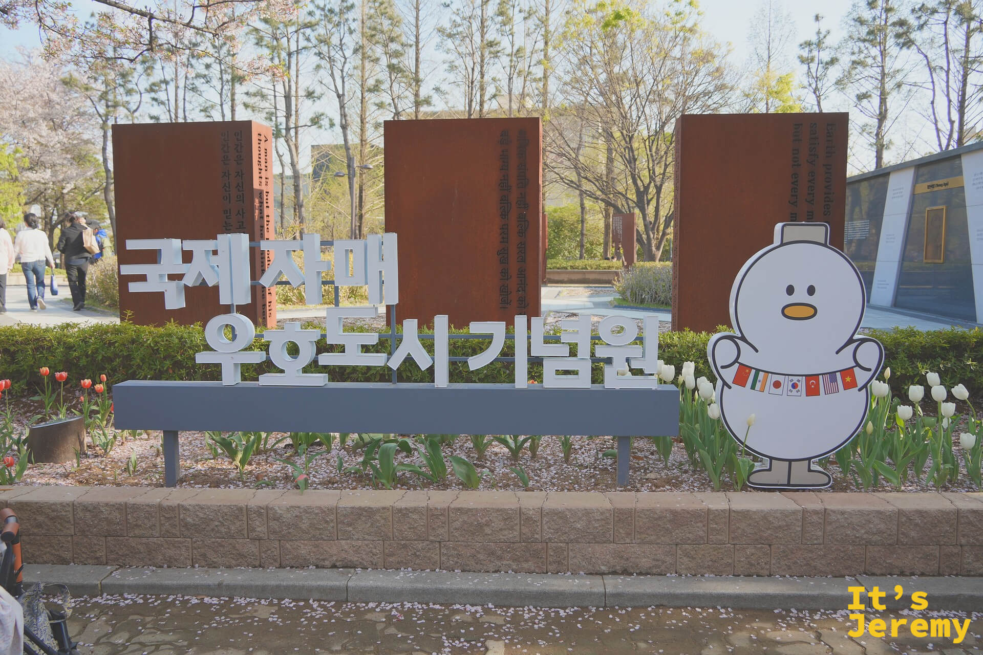 國際姊妹城市紀念苑入口看板與可愛吉祥物立牌，後方鬱金香盛開