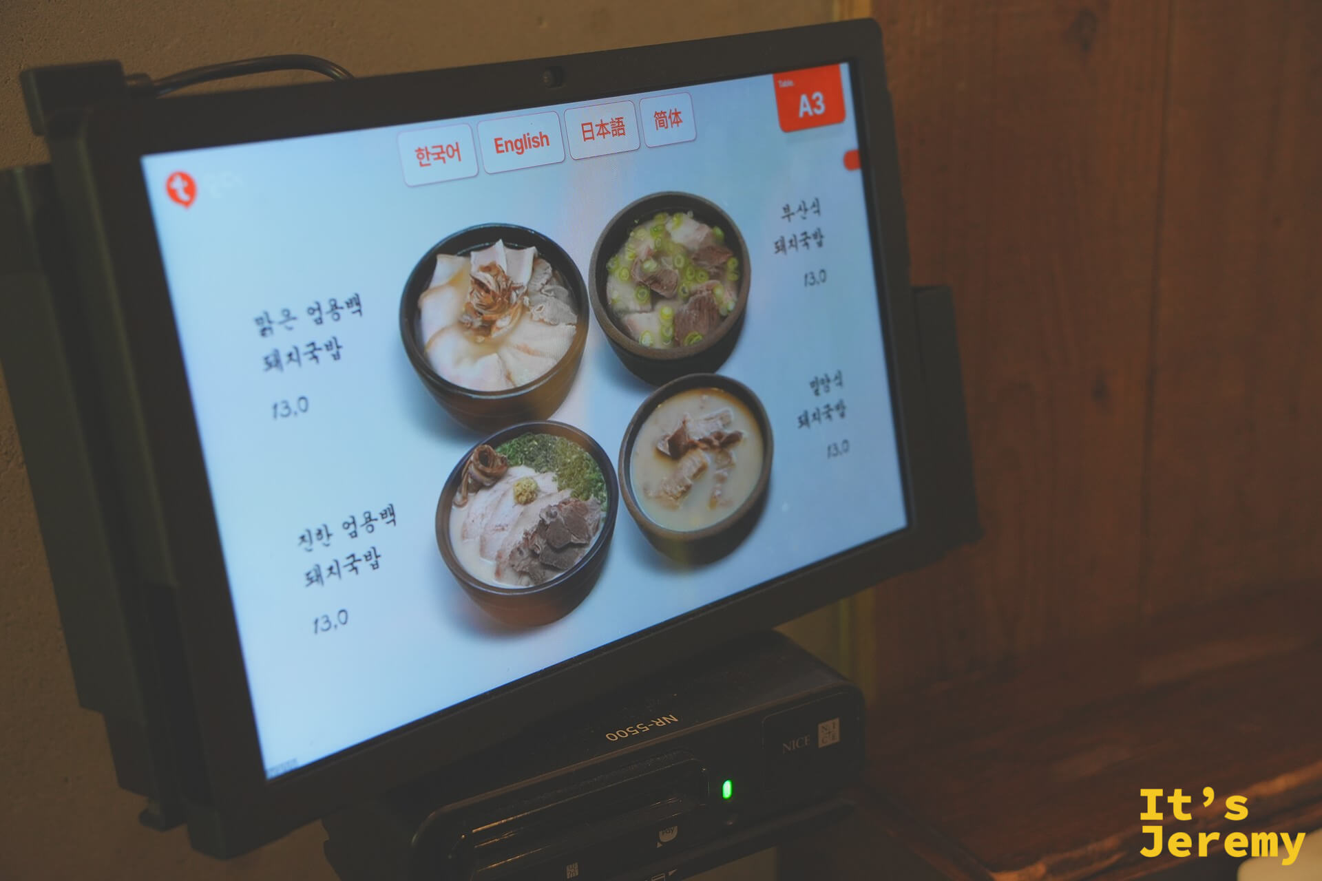 座位桌上的平板點餐機，顯示四款豬肉湯飯選項與照片，介面提供韓英日中四種語言