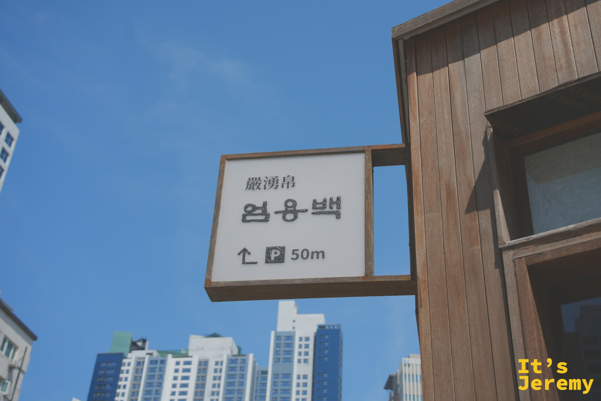 店外路標指示，漢字「嚴湧帛」清晰可見，藍天下簡潔俐落的木框招牌