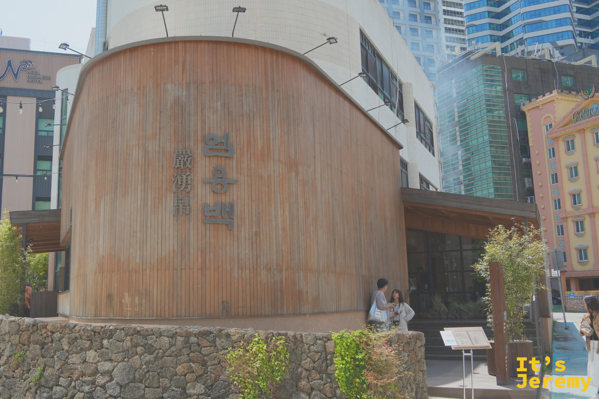 嚴湧帛海雲台店外觀，曲面木質外牆上嵌著嚴湧帛漢字招牌，背後是海雲台高樓群