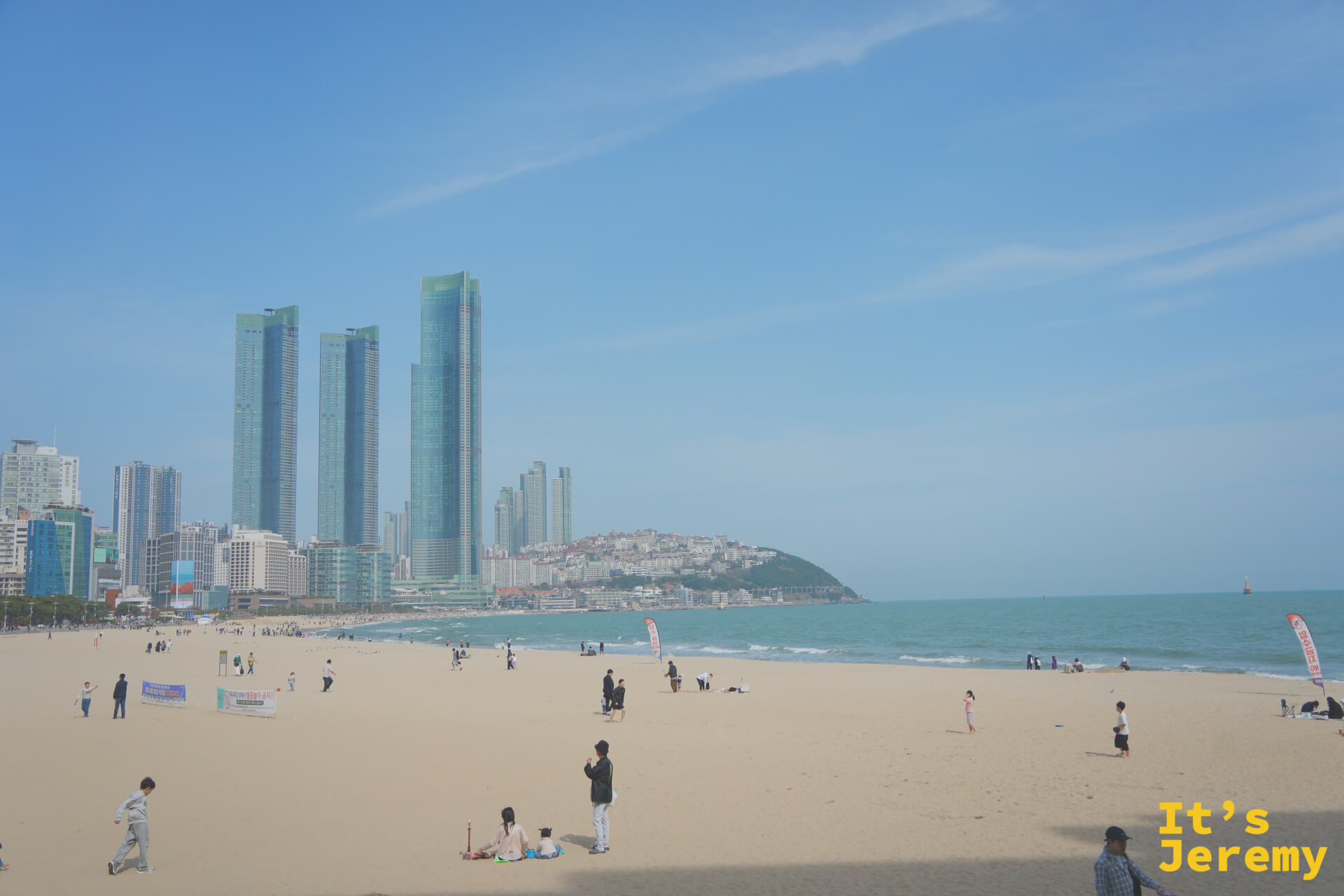 站在沙灘中段回望,LCT 雙塔與東白島岬角框出海雲台最經典的明信片畫面