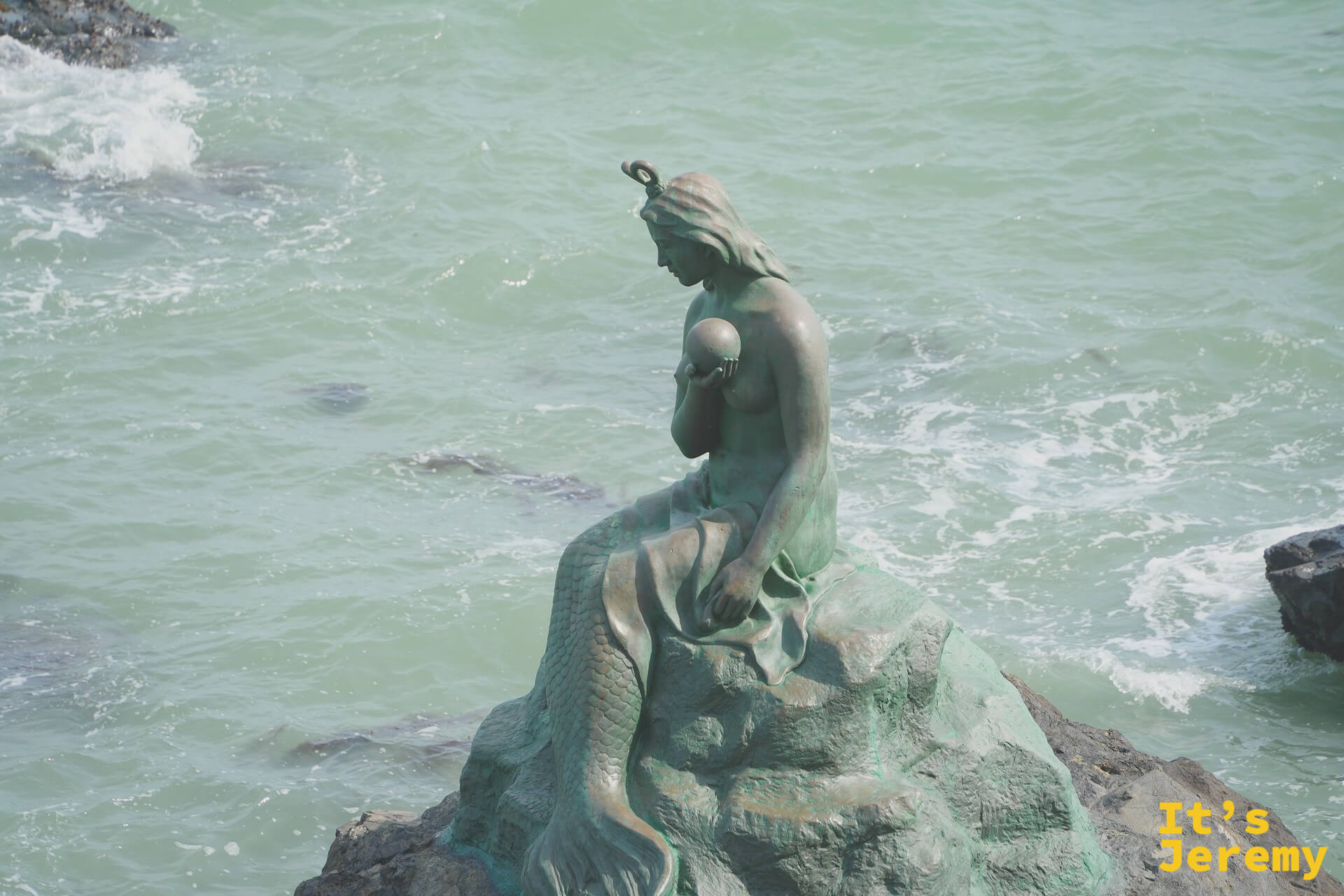 冬柏島人魚銅像，坐在礁石上望向大海，墨綠色氧化銅質地與海浪相映
