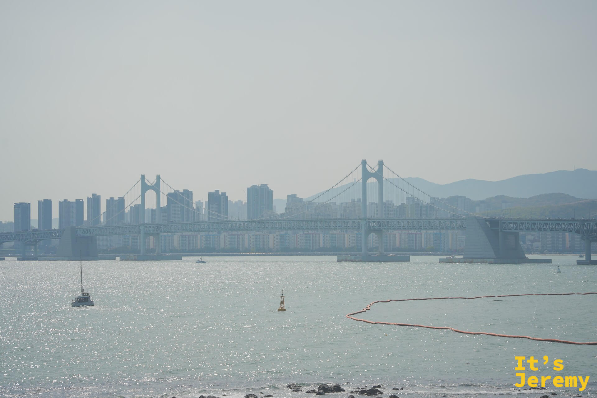 站在礁石岬角，遠眺廣安大橋的完整懸索輪廓，水面波光閃爍