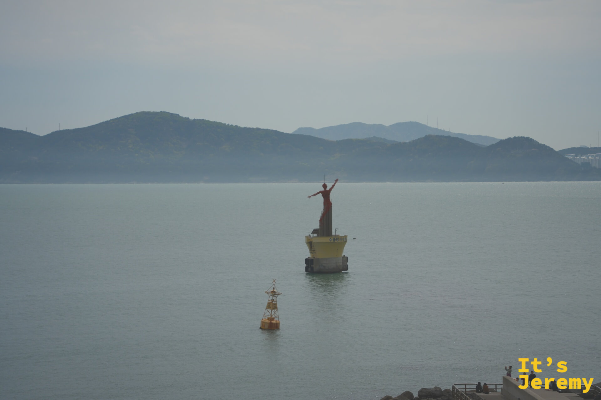 從咖啡廳窗邊遠眺，防波堤末端的紅色女神守護像佇立海中