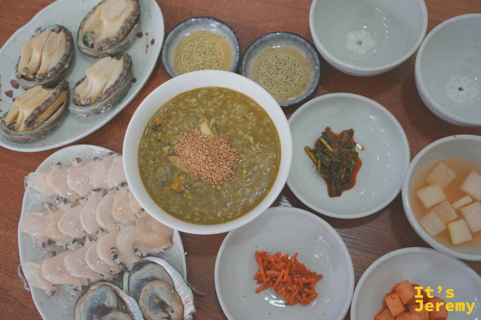 全桌俯拍:左方찐전복蒸鮑魚、中央전복죽鮑魚粥、下方전복회刺身,小菜圍繞四周,主食配角各就各位