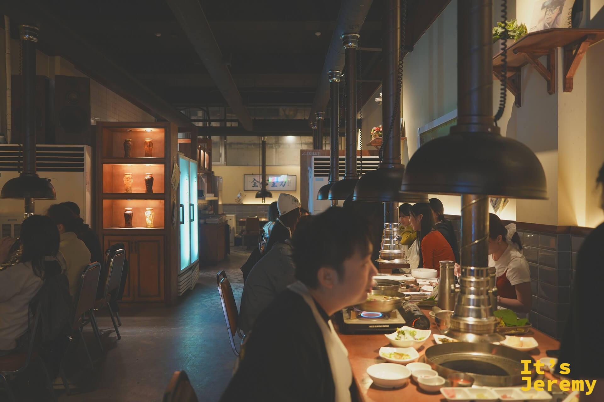餐廳內部氛圍：黑鐵吊燈、木桌、排氣管道，工業復古調性在暖燈下顯得格外溫潤