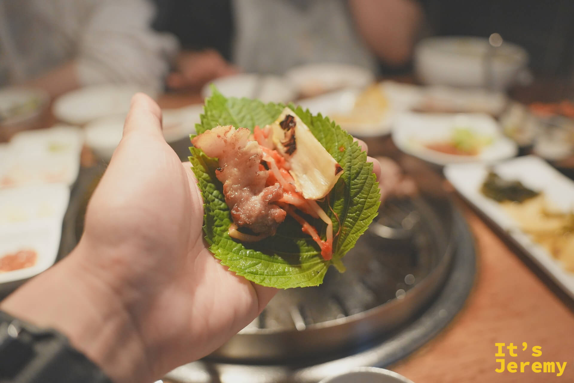 一手捧起的紫蘇葉包肉：五花肉、大蒜、泡菜一起包進葉片，是這頓飯的精華句點
