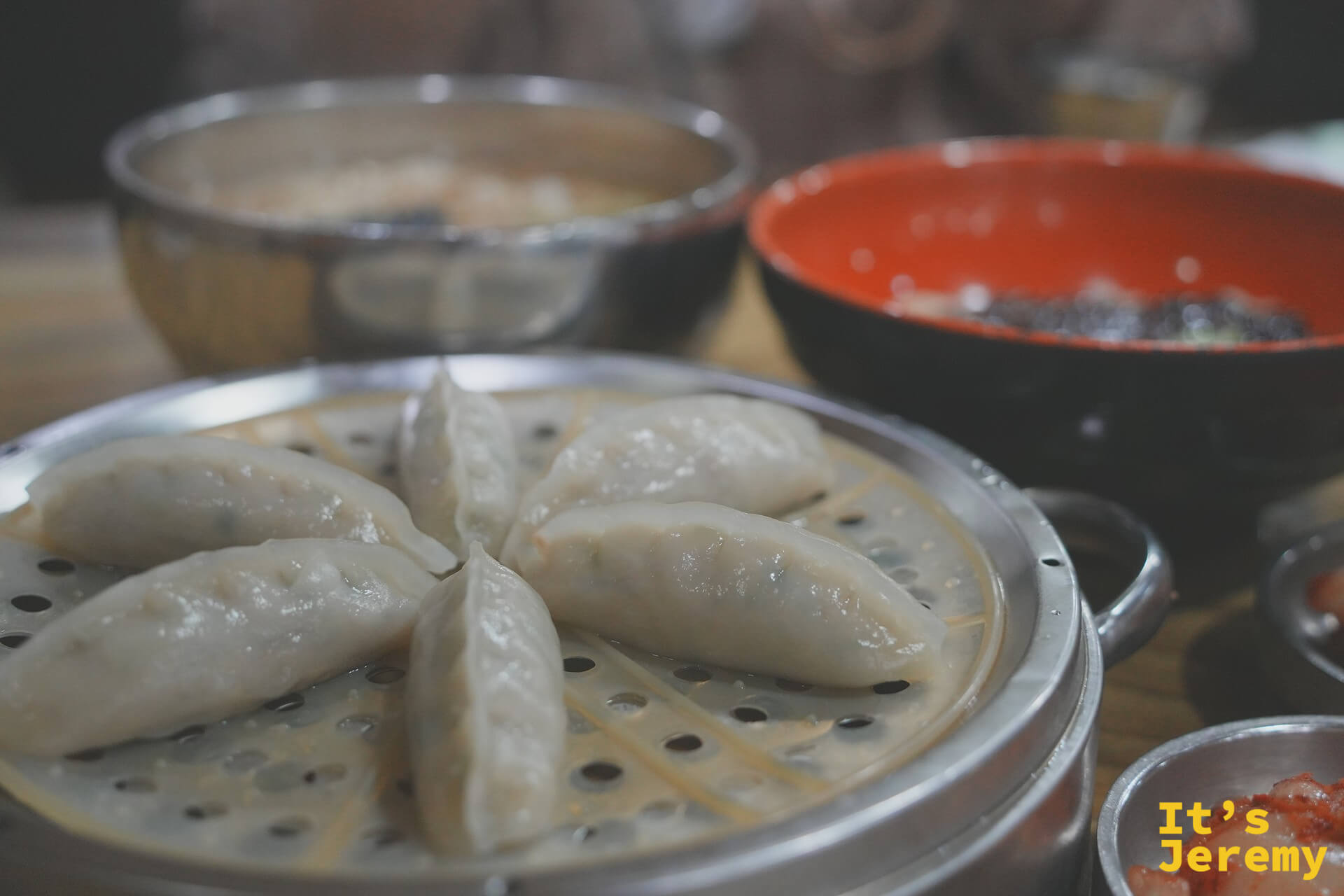 水餃近景,後方模糊可見칼국수銀碗與짜장면紅碗