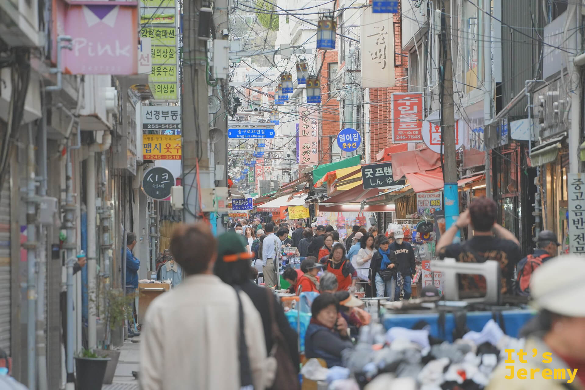 國際市場另一條巷弄，人流從食物攤和服飾攤之間擠過去，攤子、招牌、傘蓋疊成一整面
