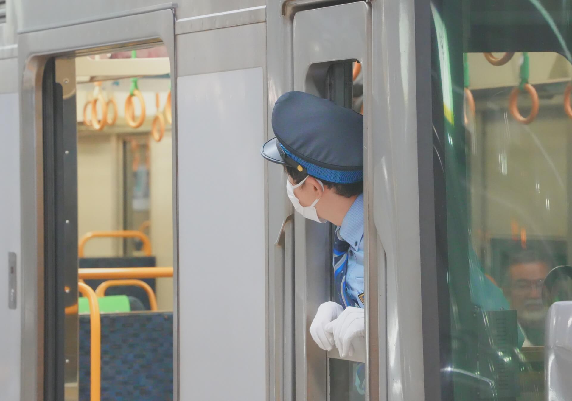 JR 站務員戴白手套從列車車門探頭確認安全的畫面