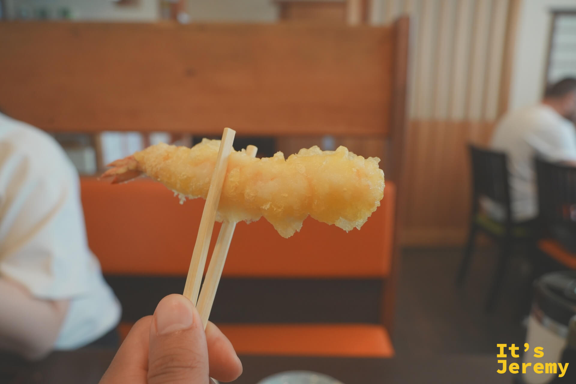 用筷子夾起一隻炸蝦,背景是志津香餐廳座席