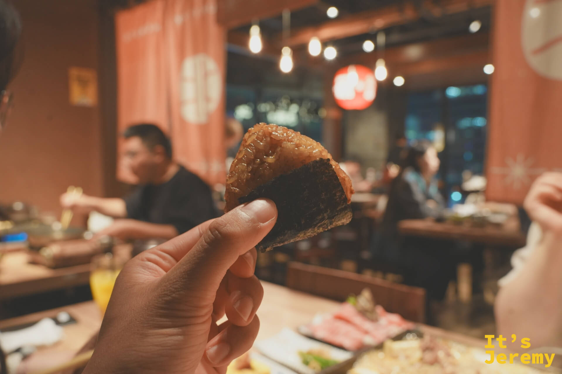 手持烤飯糰，展示焦香表面與餐廳氛圍