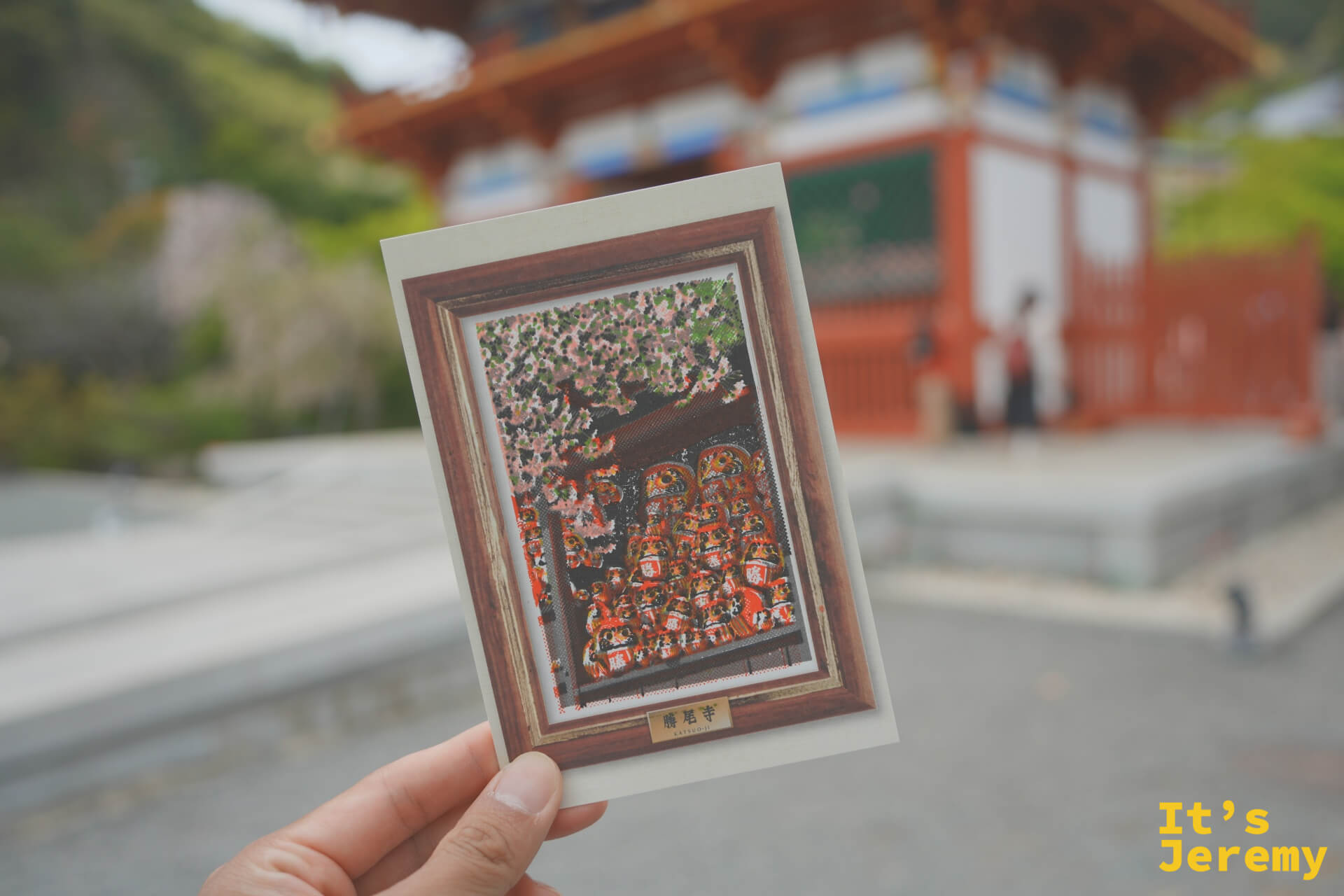 手持完成版明信片,背景是勝尾寺山門