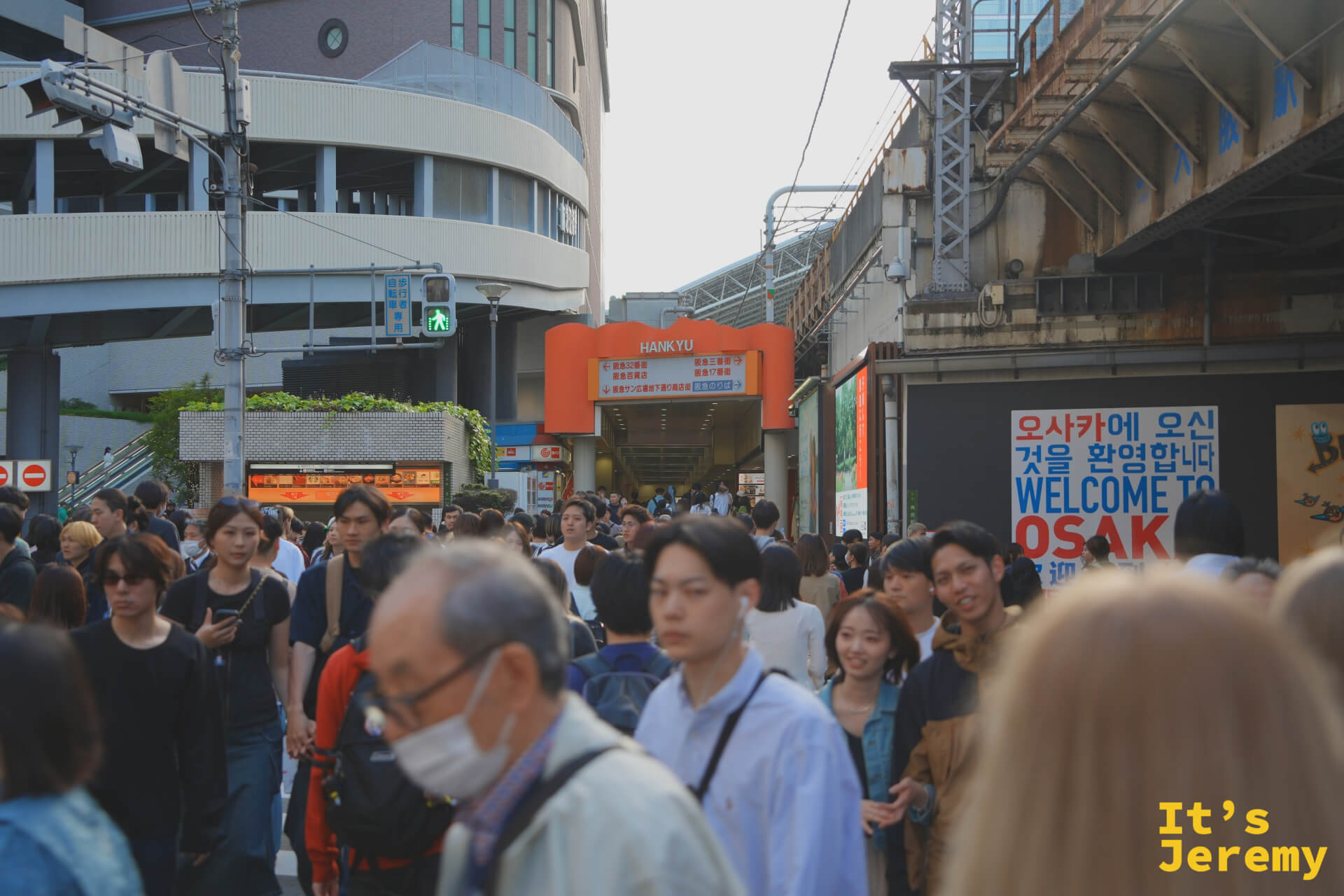 梅田阪急百貨前的人潮，背景 WELCOME TO OSAKA 看板清楚可見，傍晚的下班流把整條街道填滿