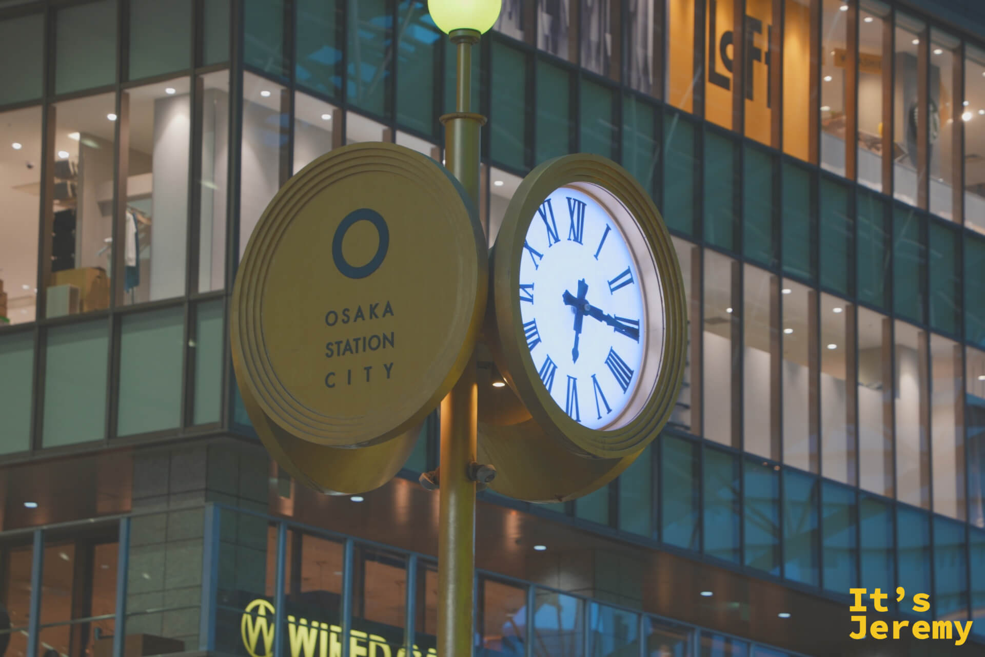 Osaka Station City 圓形時鐘路燈，入夜亮起，背後是 Loft 的玻璃帷幕，這一帶是梅田逛街最標誌性的地標之一
