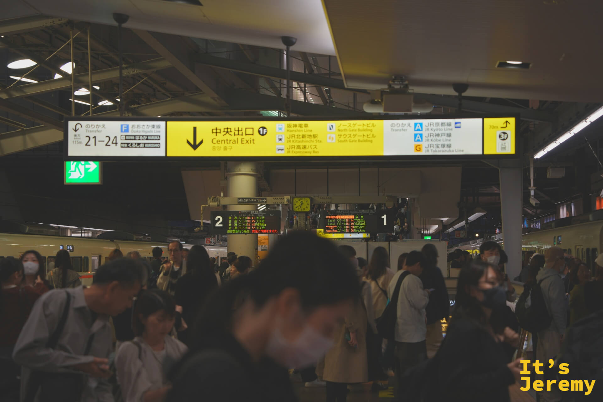 JR 大阪站月台，中央出口的黃色大型指示看板懸在頭頂，入夜的月台依然擠滿人