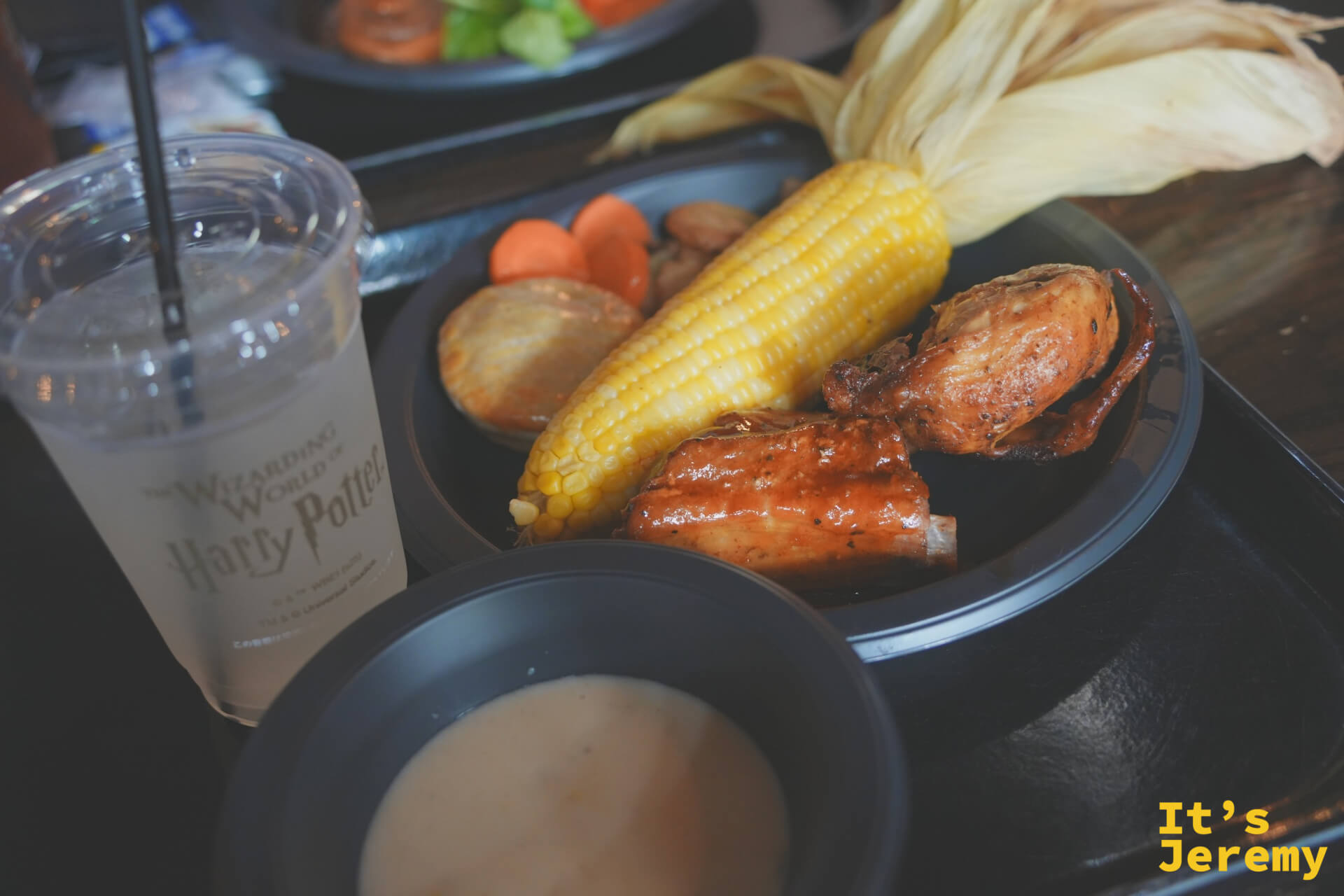 三本の箒™ 烤雞與豬肋排套餐，黑色餐盤盛著烤雞塊、豬肋排、玉米、馬鈴薯，旁邊是 Harry Potter 主題的冰杯