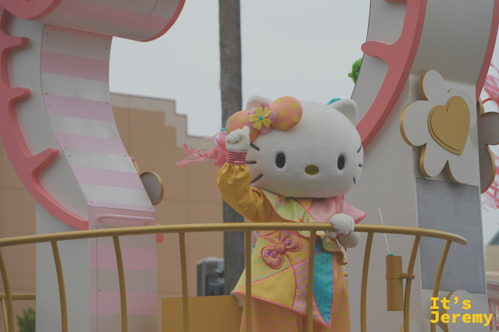 Hello Kitty 站在花車上揮手，黃色和服配上花朵頭飾，是一個很少見的特別造型