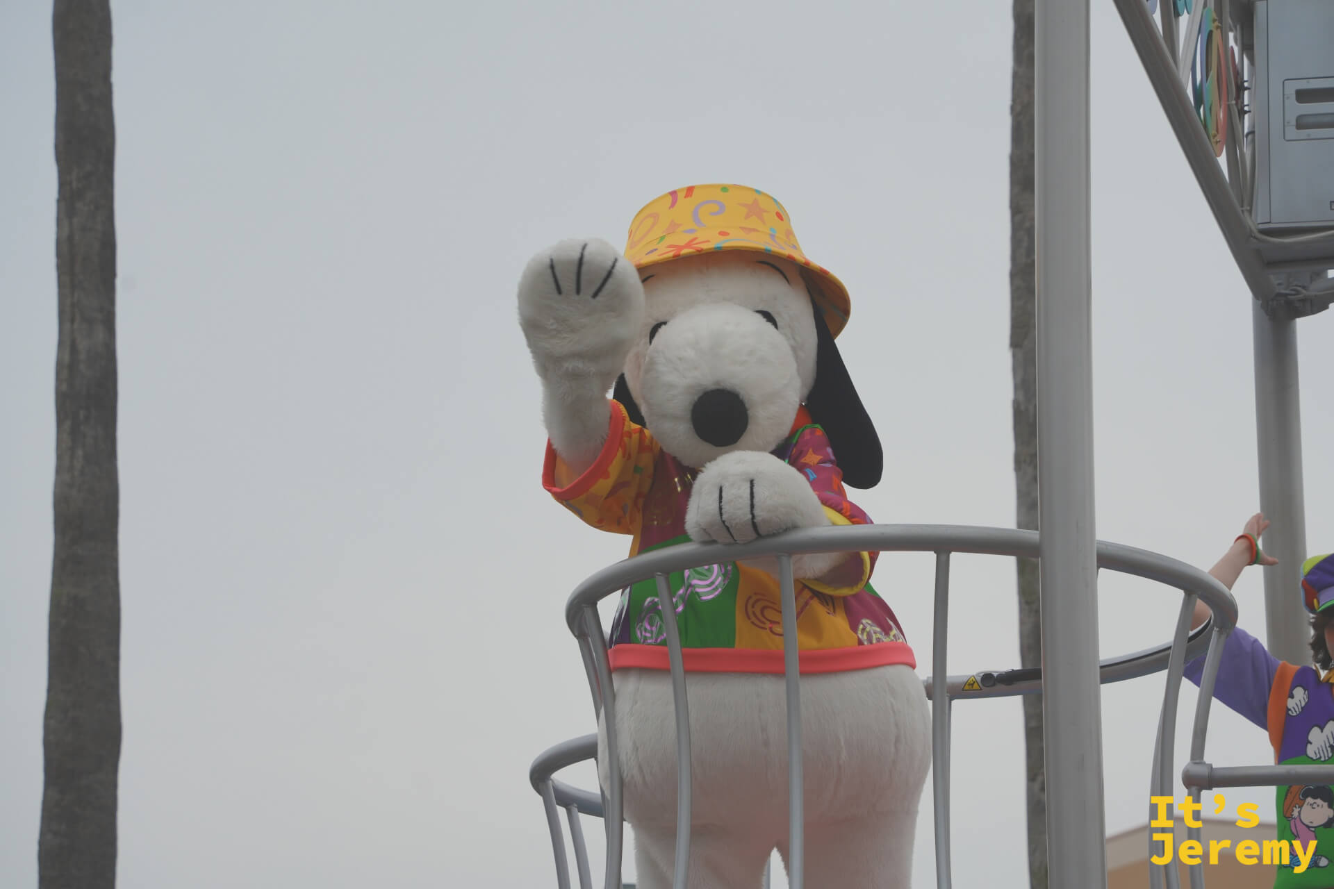 Snoopy 站在高處向觀眾揮手，身穿黃色橘色夏威夷衫，搭配黃色水桶帽