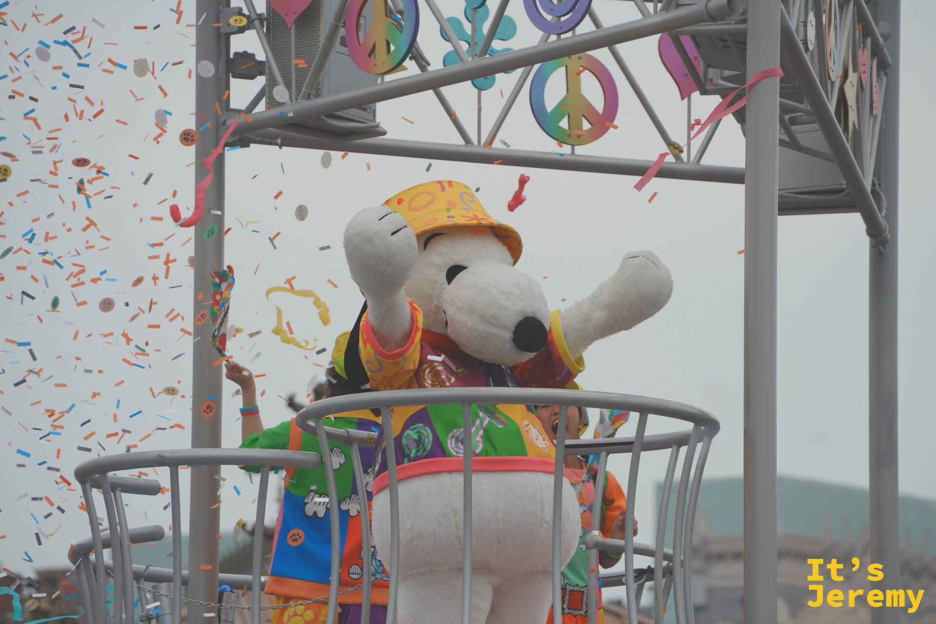 Snoopy 在彩帶飛舞中揮舞雙手，背景是五顏六色的和平符號裝飾