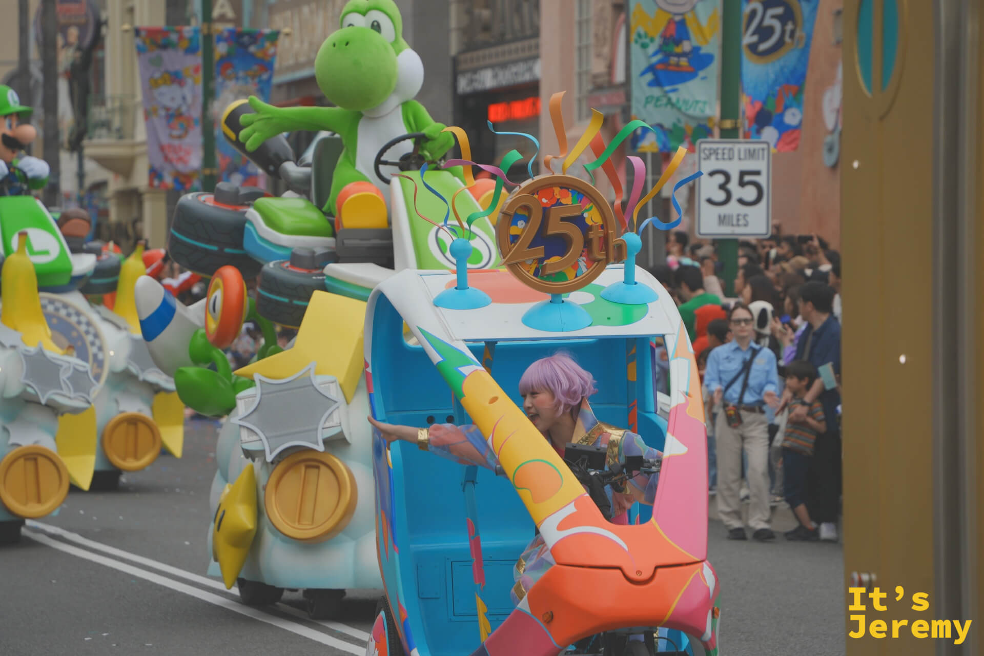 Mario Kart 花車全景，Yoshi 駕著綠色賽車在前，25th 金色標誌懸掛花車頂部，觀眾沿著街道排成人牆