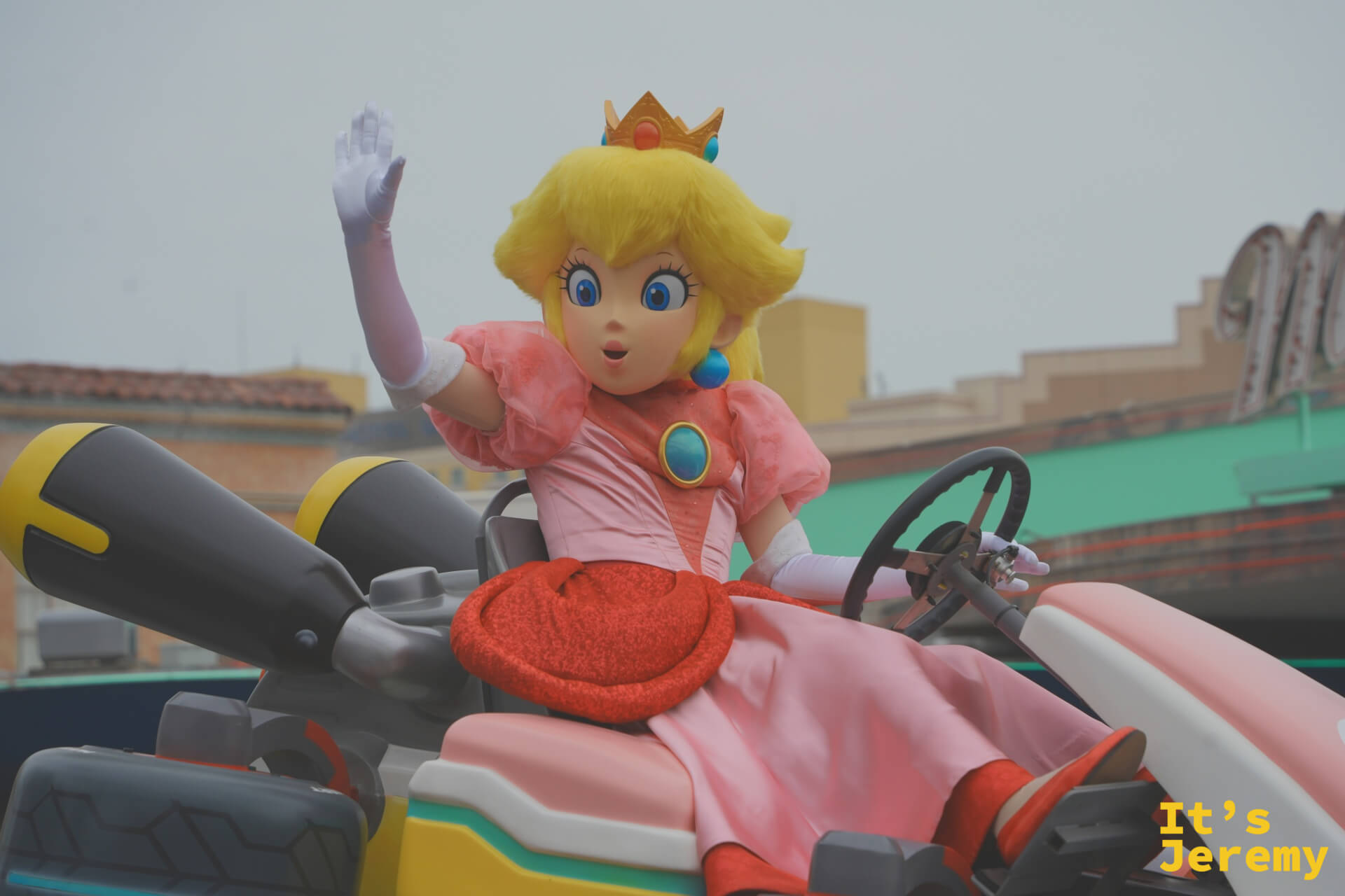 Princess Peach 特寫，粉色蓬裙、白色手套、金色皇冠，一手揮向觀眾，神情既優雅又生動