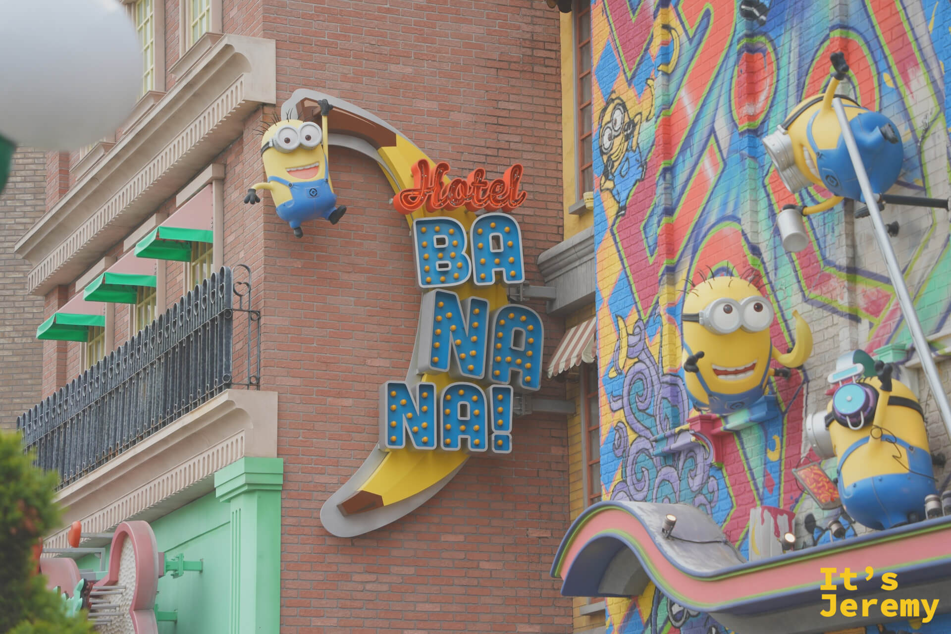「Hotel Banana」霓虹招牌，一隻 Minion 掛在香蕉形狀的招牌上，整面建築牆上都是 Minion 的插畫