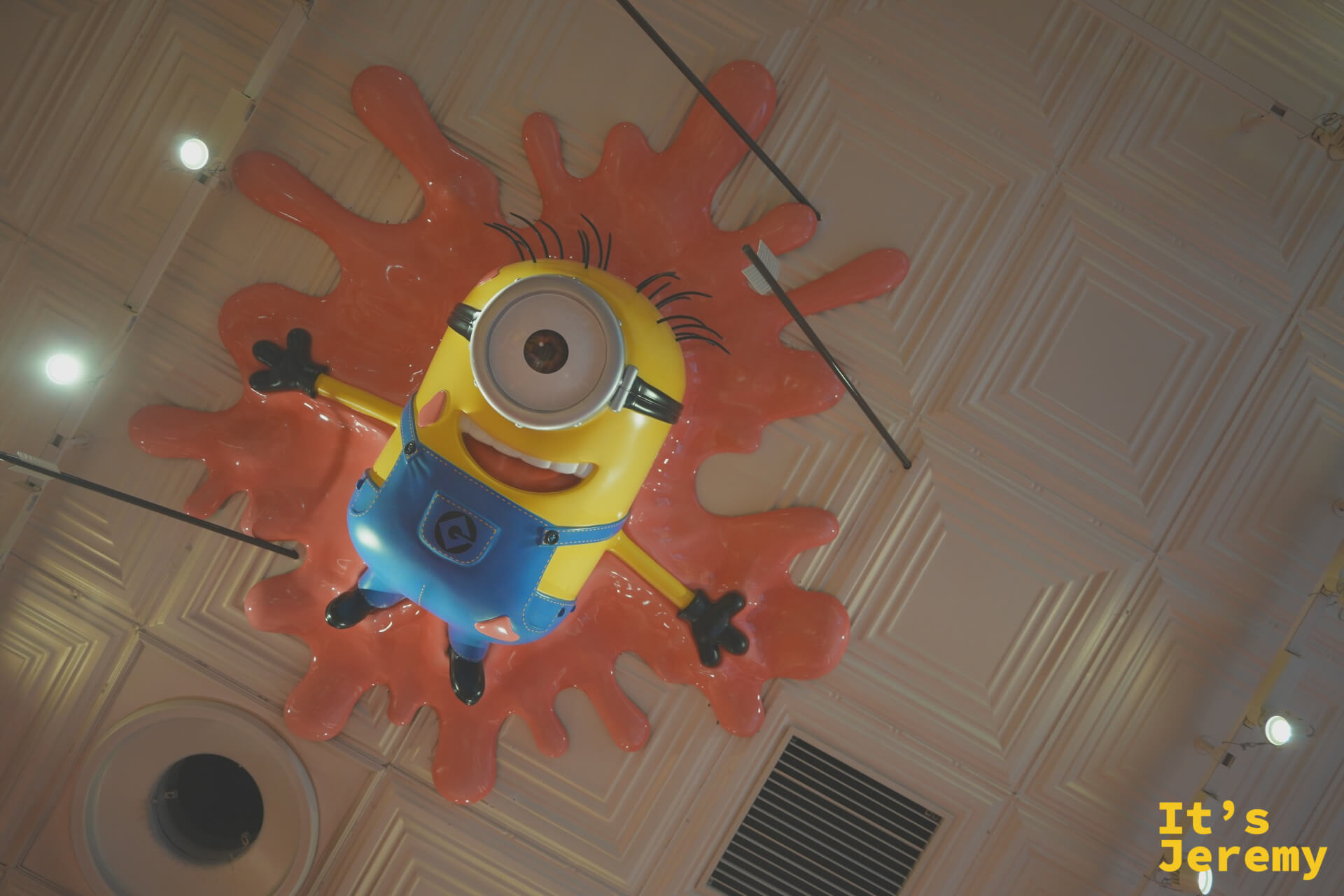 一隻單眼 Minion 被嵌在天花板上，像是剛剛撞上去一樣，是整個區域最有幽默感的裝置之一