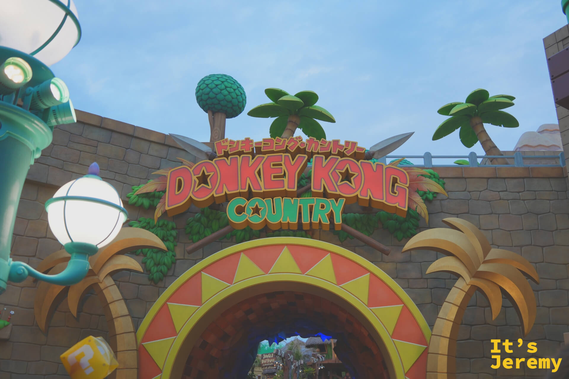 Donkey Kong Country 的入口拱門，招牌以紅色粗體字呈現，兩側是可可椰子樹造型裝飾