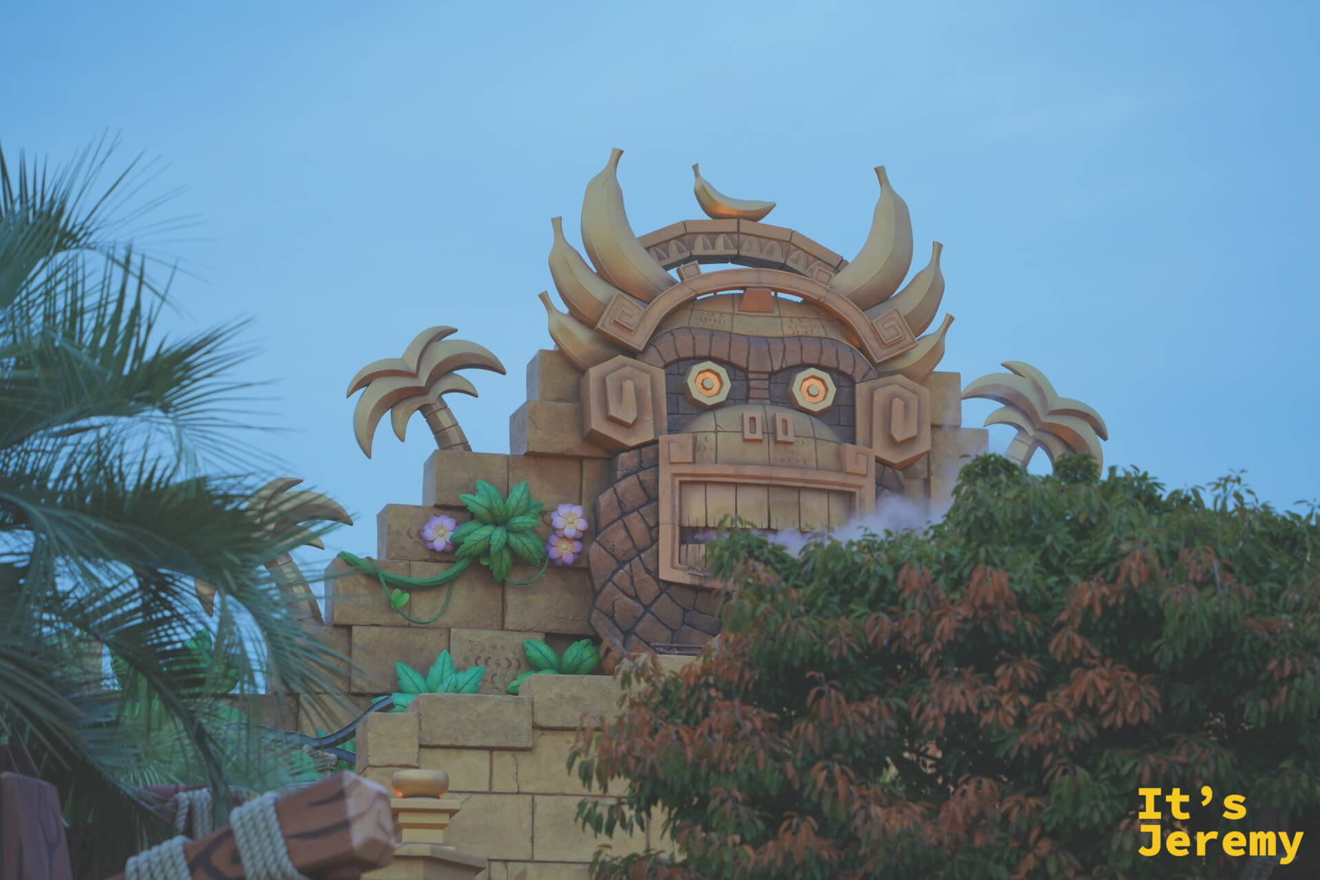 Tiki Tong 神像建築，從棕櫚樹葉隙間望去，橘色眼珠搭配香蕉圖騰的石雕建築令人印象深刻