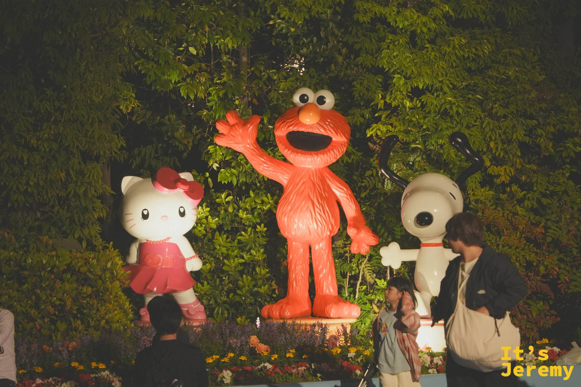 Hello Kitty、Elmo 與 Snoopy 的雕像圍繞在花圃燈光中，在深夜裡靜靜等著與每一個訪客道別