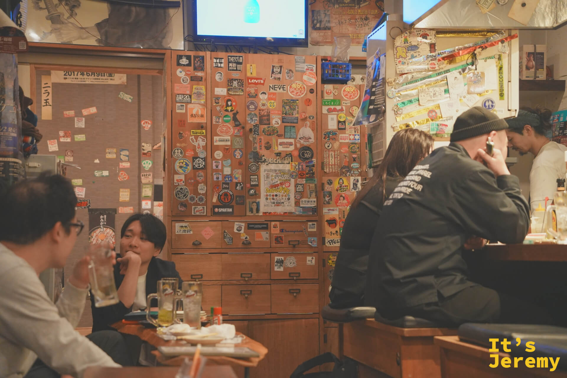 店內全景，座位幾乎坐滿，外國旅客與本地客人比肩而坐，電視開著
