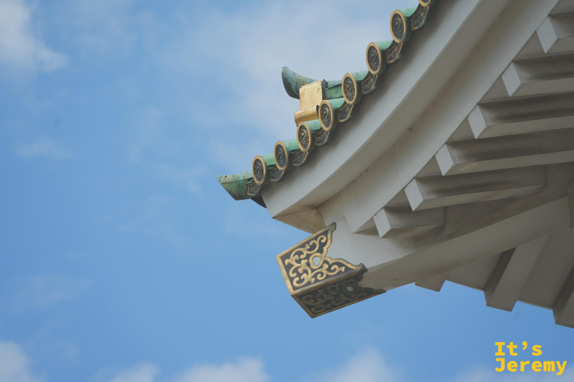 天守閣屋簷仰角特寫，翠綠陶瓦與金色卷草紋清晰可見